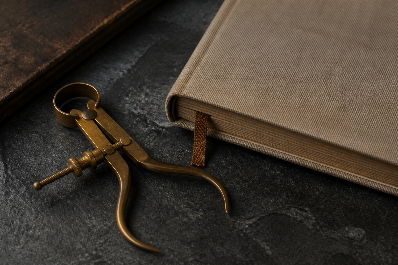 Brass measuring calipers and a linen journal on a dark slate table.